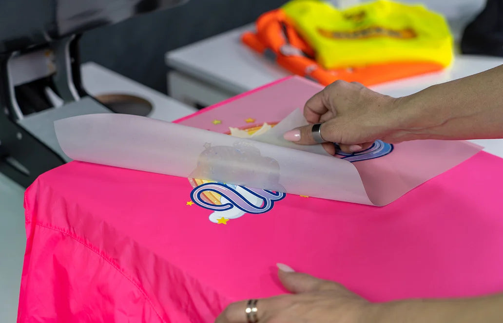 Female hand peeling off a DTF transfer from a pink t-shirt in a print shop